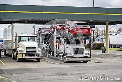 Powerful industrial big rig semi trucks with dry van and car hauler loaded semi trailers standing on the truck stop parking lot Stock Photo