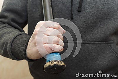 Hand in hoodie grips the shabby hilt of a black wooden baseball bat Stock Photo