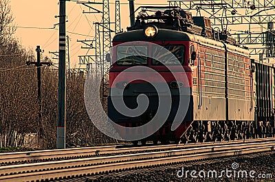 A powerful red diesel locomotive pulls a long freight train along the tracks Stock Photo