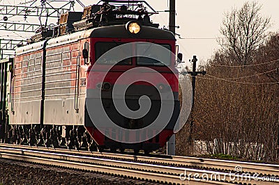 A powerful red diesel locomotive pulls a long freight train along the tracks Stock Photo
