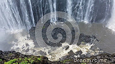 Powerful streams of Victoria Falls fall into the gorge. At the bottom are black stones. Stock Photo