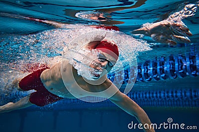 Powerful strokes pf swimmer developing speed. Young swimming male athlete in motion, in cap and goggles in swimming pool Stock Photo