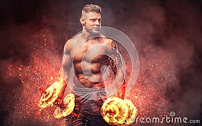 Handsome shirtless tattooed bodybuilder with stylish haircut and beard, wearing sports shorts, posing in a studio. Fire Stock Photo