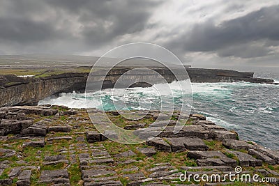 Powerful waves hist rocks at the bottom of cliff. Inishmore, Aran islands, county Galway, Ireland. Cloudy sky. Nobody. Nature Stock Photo