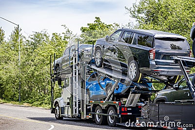 Powerful white big rig car hauler semi truck transporting cars on the two level modal semi trailer running on the road with trees Stock Photo