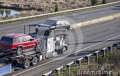 Powerful white big rig semi truck car hauler transporting cars on the combined multilevel semi trailer running on the straight Stock Photo