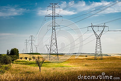 Powerlines hanging from tall steel towers overlooking natural grasslands in rural Alberta near Calgary Stock Photo