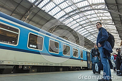 A guy waiting for the train at the Prague main train station with people boarding the blue train of Ceske Drahy Editorial Stock Photo
