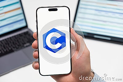 C logo on the screen of smartphone in mans hand on the workplace background Editorial Stock Photo
