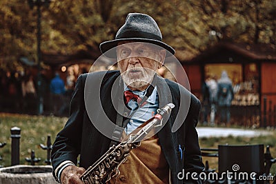 Prague, Czech Republic/ 1 November 2019: Old street musician with sax playing on the street, close up portrait. Tourist attraction Editorial Stock Photo