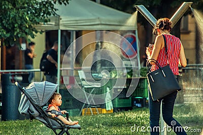 Mother cools down sun in public mist machine at Park Editorial Stock Photo