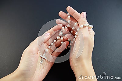 Praying on the rose garden, the hands of a young virgin with a rosary close-up on a black background. Stock Photo