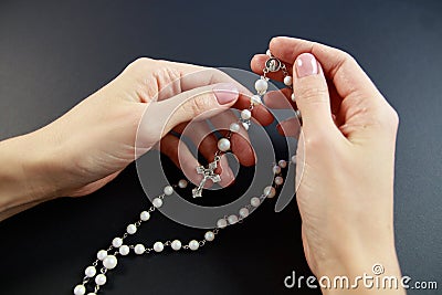 Praying on the rose garden, the hands of a young virgin with a rosary close-up on a black background Stock Photo