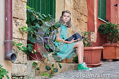 Pre-adolescent schoolgirl with a book sitting on steps of outdoor Stock Photo