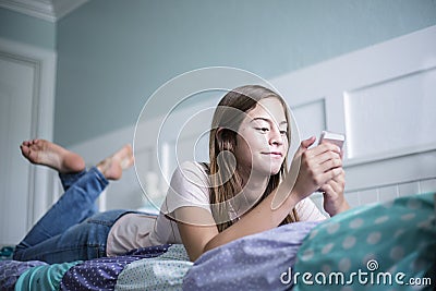 Pre-adolescent teen girl texting on a smartphone lying in bed at home Stock Photo