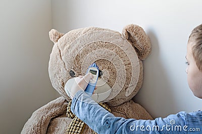 Pre-school boy is looking after his sick teddy bear. Boy is measuring temperature on its forehead with modern digital thermometer Stock Photo