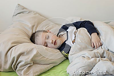 Pre-school sick boy with closed eyes lying in bed with a digital thermometer Stock Photo