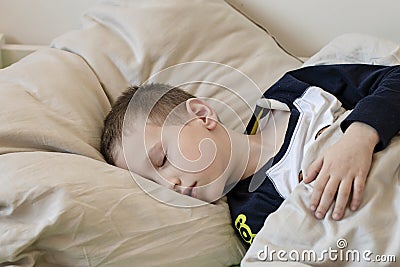 Pre-school sick boy with closed eyes lying in bed with a digital thermometer Stock Photo