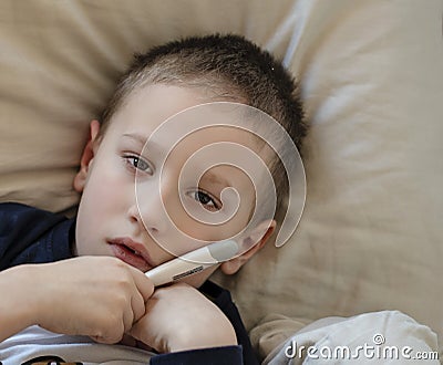 Pre-school sick boy lying in bed with a digital thermometer in hand and looking into camera Stock Photo