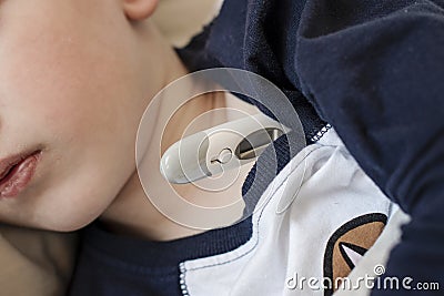 Pre-school sick boy lying on pillow in bed with a digital thermometer. Ill boy is measuring body temperature - close up Stock Photo