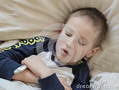 Pre-school sick boy in pyjama lying in bed with a digital thermometer in hand Stock Photo