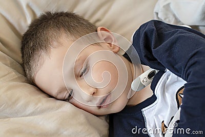 Pre-school sick boy in pyjama lying in bed with a digital thermometer Stock Photo