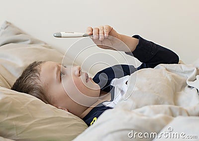 Pre-school sick boy in pyjama lying in bed and looking at digital thermometer Stock Photo