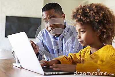 Pre teen girl African American girl using a laptop computer sitting at table in the dining room with her home tutor, close up, se Stock Photo