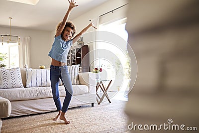 Pre-teen girl dancing and singing along to music on TV in the living room at home, three quarter length Stock Photo