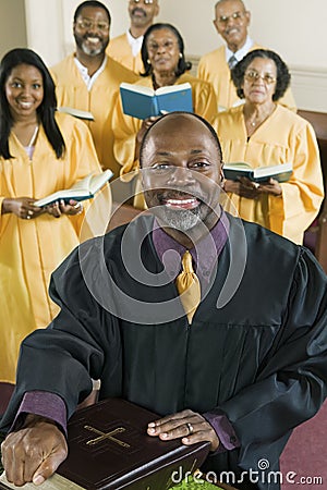 Preacher With Bible While Choir Standing In Background At Church Stock Photo
