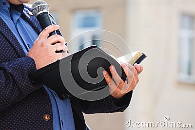 A preacher with a microphone in his hand holds a Bible and reads a passage from it_ Stock Photo