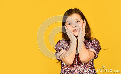 Precious face. Child pulls her cheeks up in affection. Girl cute smile on yellow background. Childhood and happiness Stock Photo