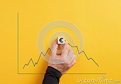 Predicting the market fluctuation in euro currency. Hand holds the wooden cube with euro symbol with an increasing and declining Stock Photo