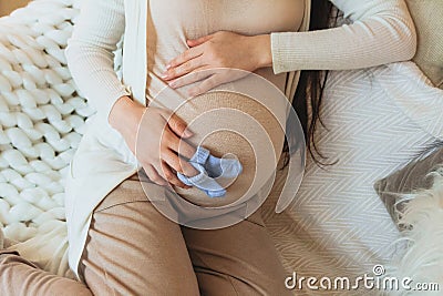 Pregnancy. Cropped photo of pregnant woman holding pair of cute blue baby socks on belly Stock Photo