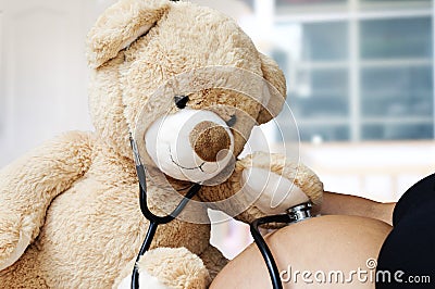 Pregnancy, medicine and healthcare concept - close up of Teddy bear playing doctor stethoscope and listens to her mother`s Stock Photo