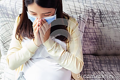 Pregnancy mother get sick of cold or flu and coughing. Young pregnant asian woman in medical mask stay alone at home for self Stock Photo