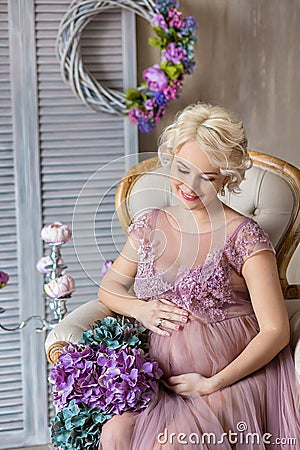 Pregnancy, motherhood and happy future mother concept - pregnant woman in airy violet dress with bouquet flowers against colorful Stock Photo