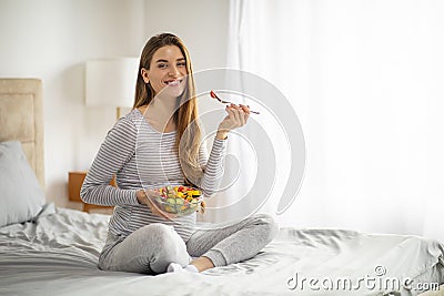 Pregnancy Nutrition. Pregnant Woman Eating Salad While Sitting On Bed At Home Stock Photo