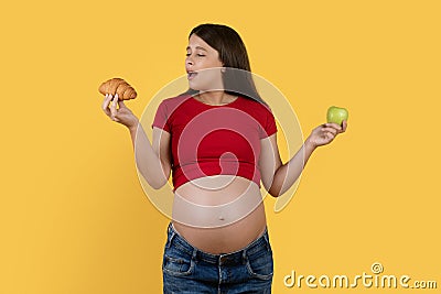 Pregnancy Nutrition. Pregnant Young Woman Choosing Croissant Instead Of Green Apple Stock Photo