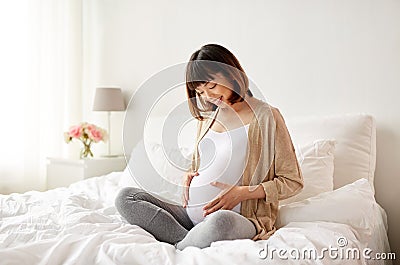 Happy pregnant asian woman sitting in bed at home Stock Photo