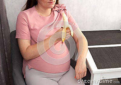A pregnant girl eats a banana in the kitchen. The concept of healthy eating vegetables and fruits rich in vitamins during Stock Photo