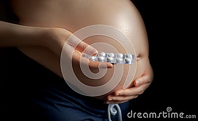 pregnant girl holding pills on the background of pregnant belly, the concept of taking drugs and vitamins Stock Photo