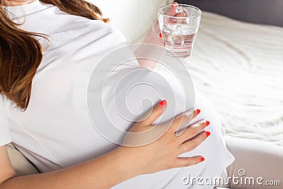 A pregnant girl with a mug of water against the background of a big belly. The concept of thirst and water balance in Stock Photo