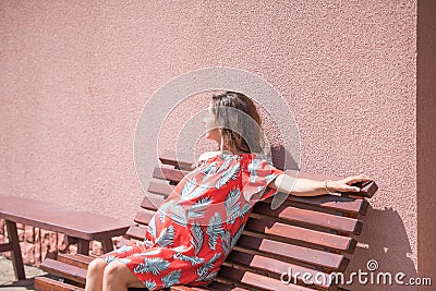 A pregnant girl is sitting on a bench. place for the inscription. Beautiful pregnant girl in dress Stock Photo