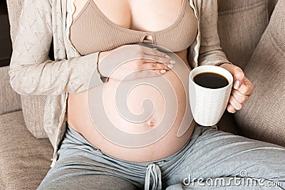 Pregnant girl sitting on sofa with coffee Cup in hand coffee. maternity morning Stock Photo