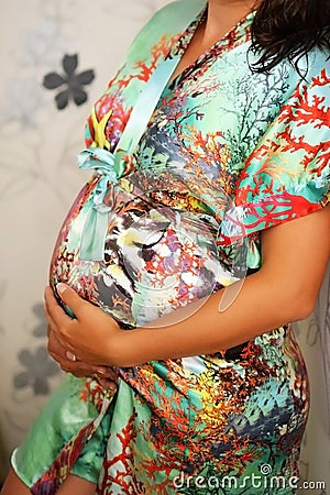 Pregnant girl in a spacious dressing gown hugs her belly with her hands Stock Photo