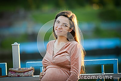 Pregnant girl walking along the promenade. Portrait of a girl with a stomach. A young girl in a summer dress walking along the Stock Photo