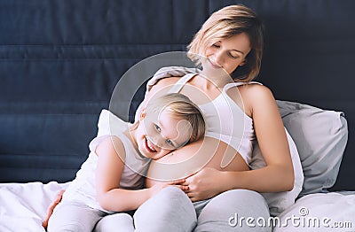 Pregnant mother and daughter resting in bed. Young woman with her first child during second pregnancy. Motherhood and parenting Stock Photo