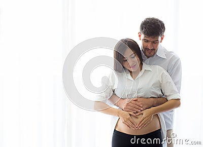 Pregnant Mother and father standing hugging holding belly heart shape with hand Stock Photo