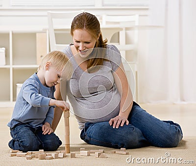 Pregnant mother watches son stack wooden blocks Stock Photo